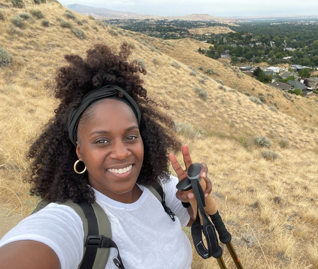 Sherika on a foothills trail with trekking poles, the valley below her